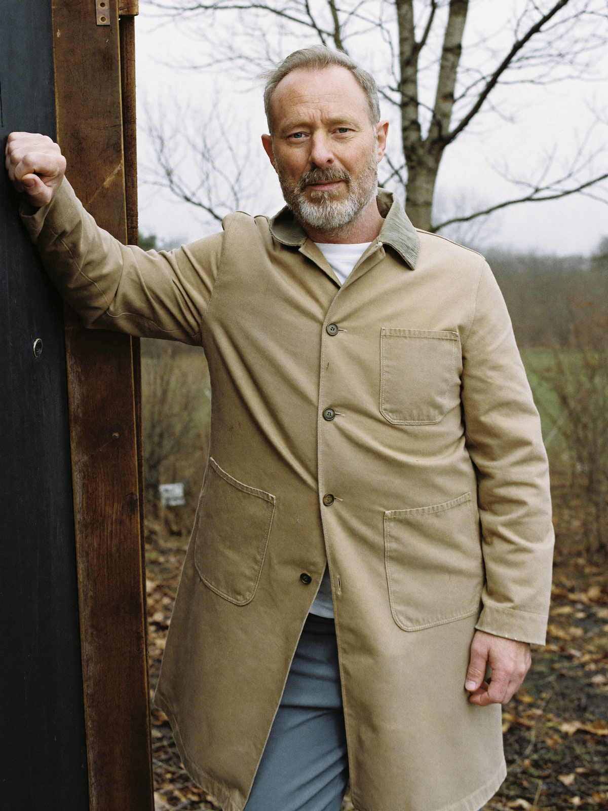 Man leaning against a barn door frame in a tan cotton duck chore coat with a corduroy collar
