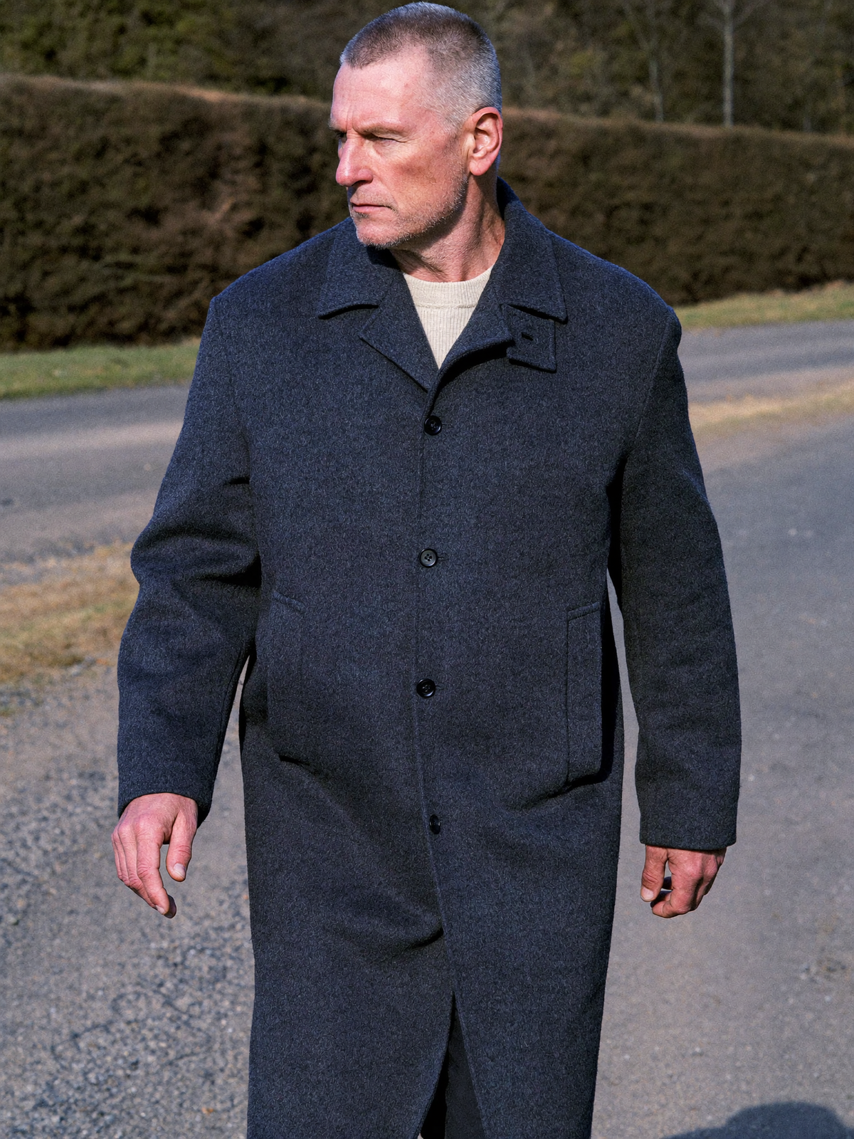 Man walking a country lane in a mid-length charcoal wool overcoat over an oatmeal sweater